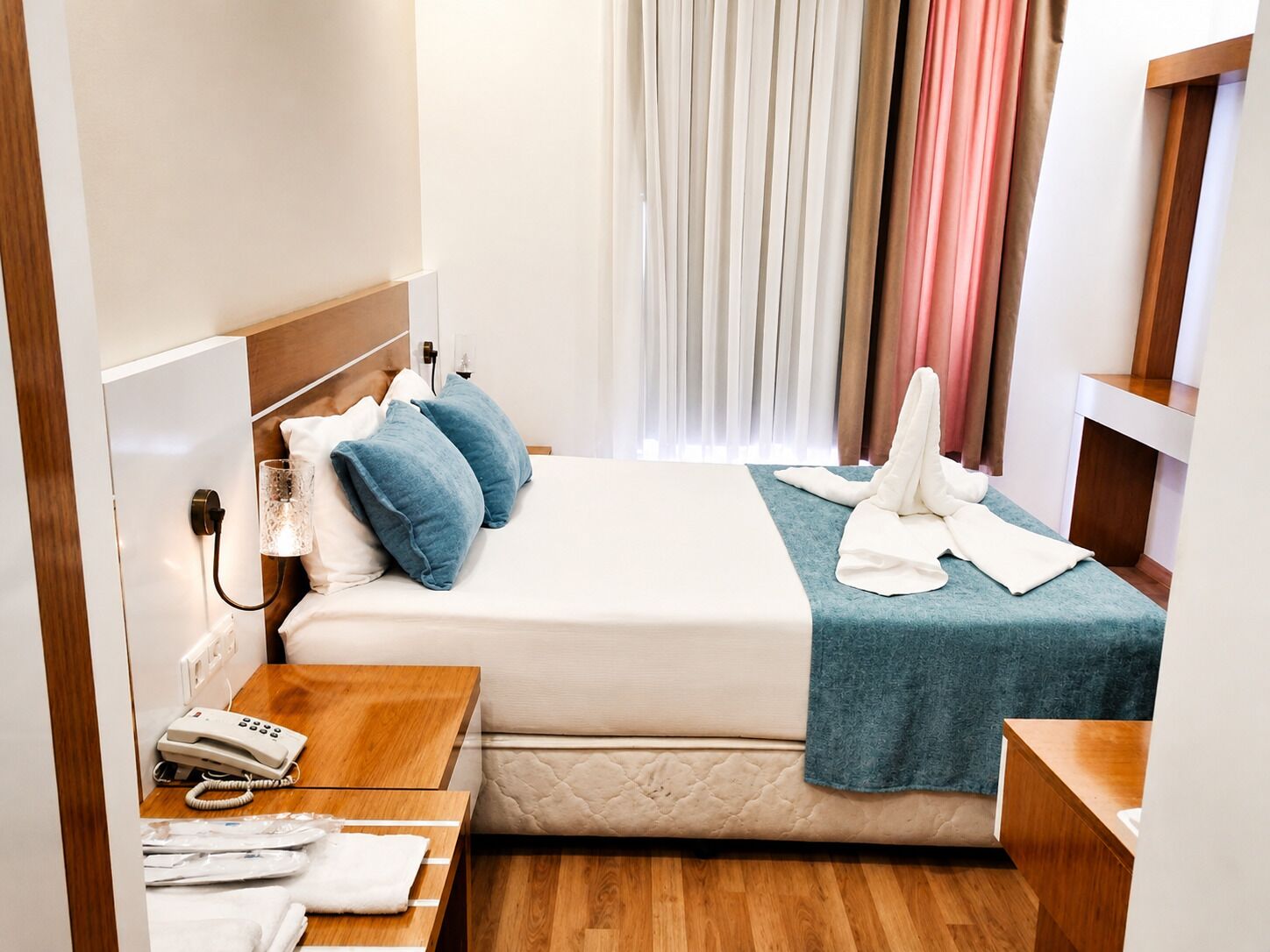 Una habitación de hotel con una cama, una mesita de noche con un teléfono, una lámpara y una ventana con cortinas.