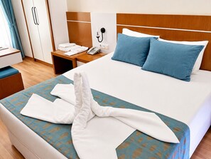 Habitación de hotel con cama, mesita de noche con teléfono, armario y ventana con cortinas.