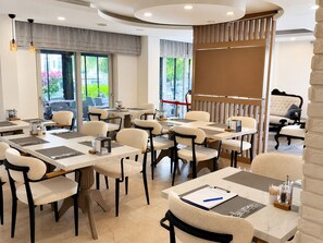 Un comedor moderno con mesas y sillas, ventanas amplias y vistas al verdor exterior.
