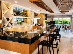 Un bar moderno con una barra alargada, varias opciones de asientos y vistas a zonas verdes.