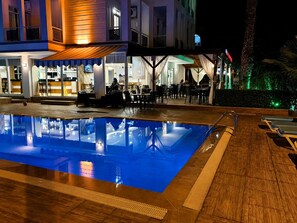 Un área junto a la piscina con piscina, sillas de descanso y un bar con asientos.