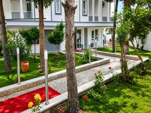 Un patio de hotel con alfombra roja, árboles y un camino empedrado.