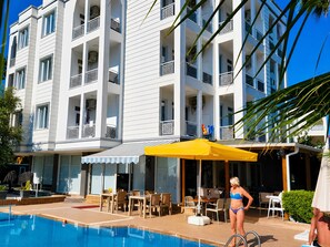 Un hotel con piscina, mobiliario exterior y un edificio de varios pisos con balcones.