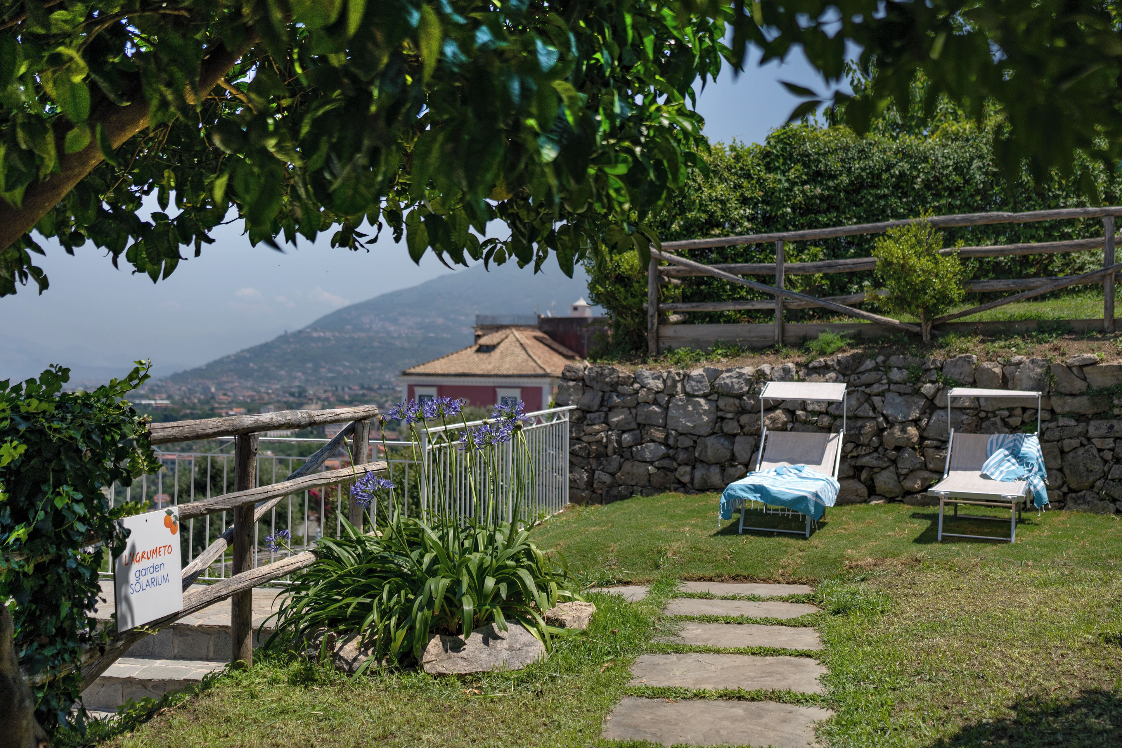 Un jardín con un muro de piedra, dos sillones de descanso y un cartel que indica un jardín llamado LAGUMETTO.