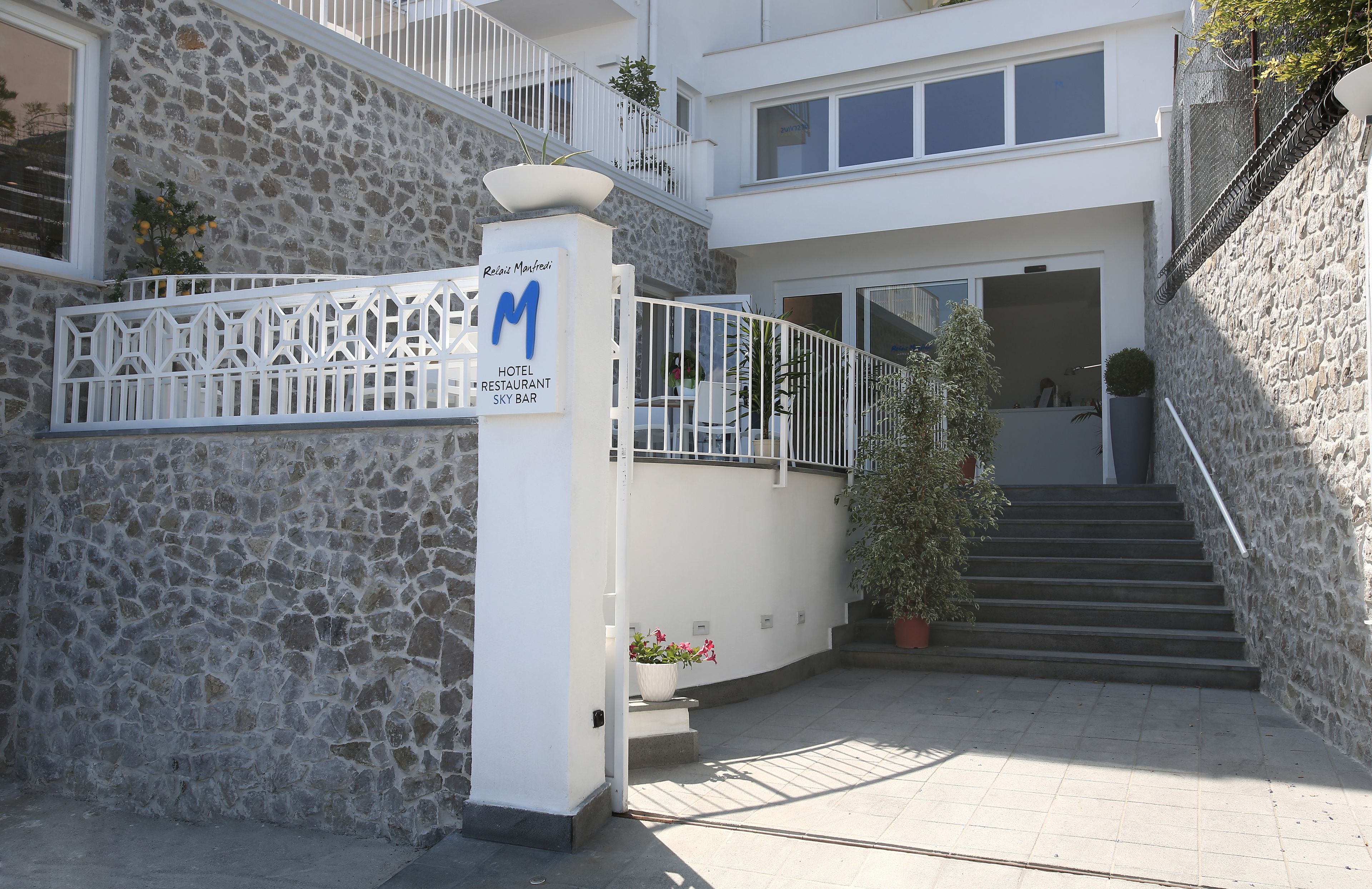 Entrada de hotel con fachada de piedra, barandilla blanca y una escalera que conduce a un nivel superior.