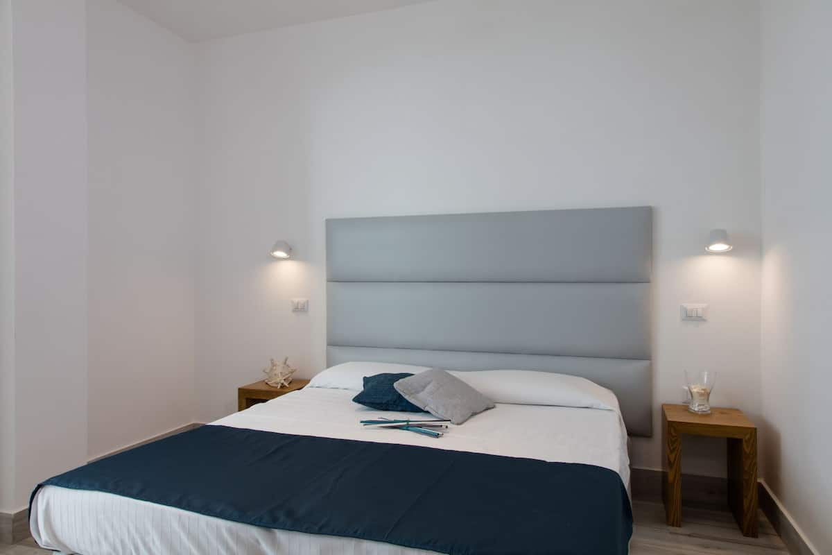 A modern bedroom with a large bed, two bedside tables, and wall-mounted lighting.