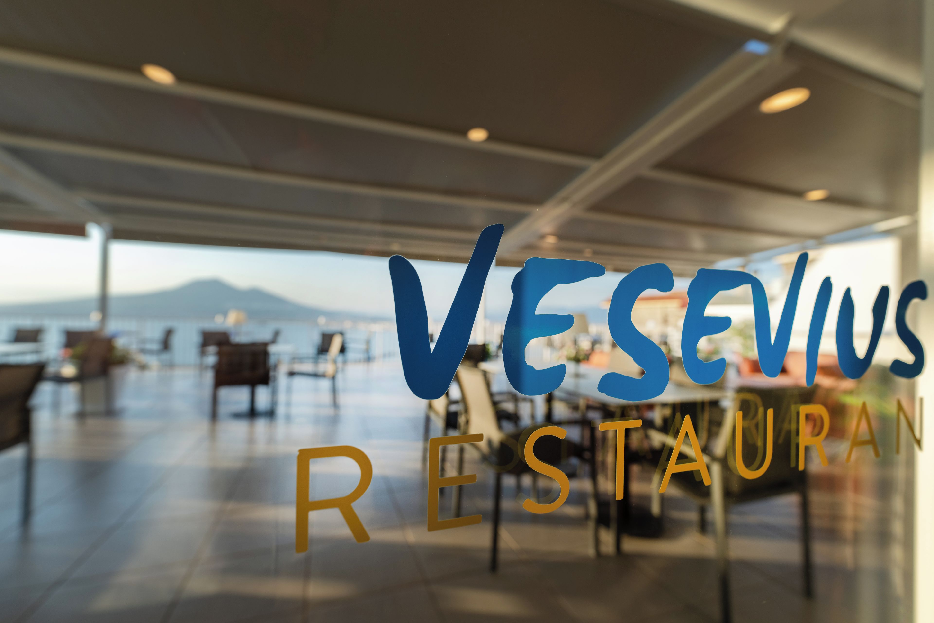 Interior de restaurante com vista para o mar e montanhas.