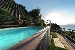 Una piscina con muelle de madera y un flotador salvavidas, rodeada de vegetación y con vistas a un cuerpo de agua.