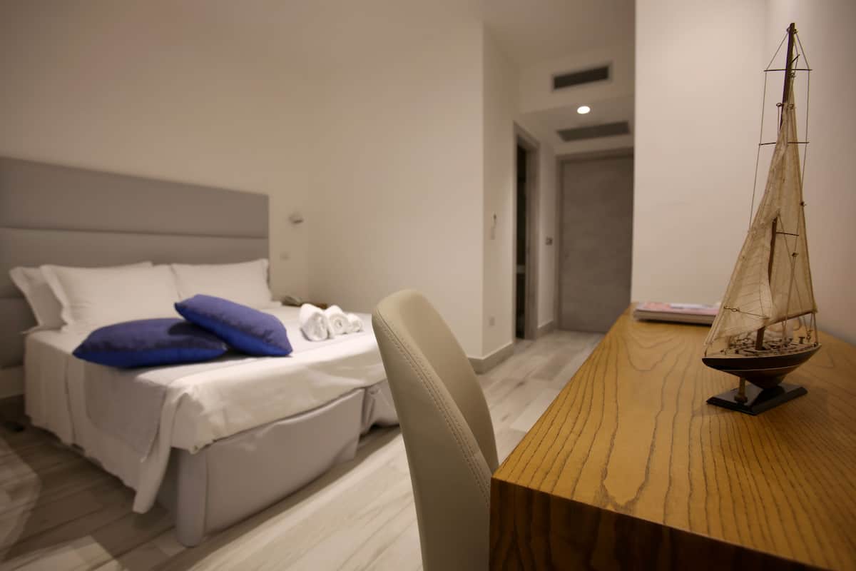 A hotel room with a bed, a wooden side table, and a model ship.
