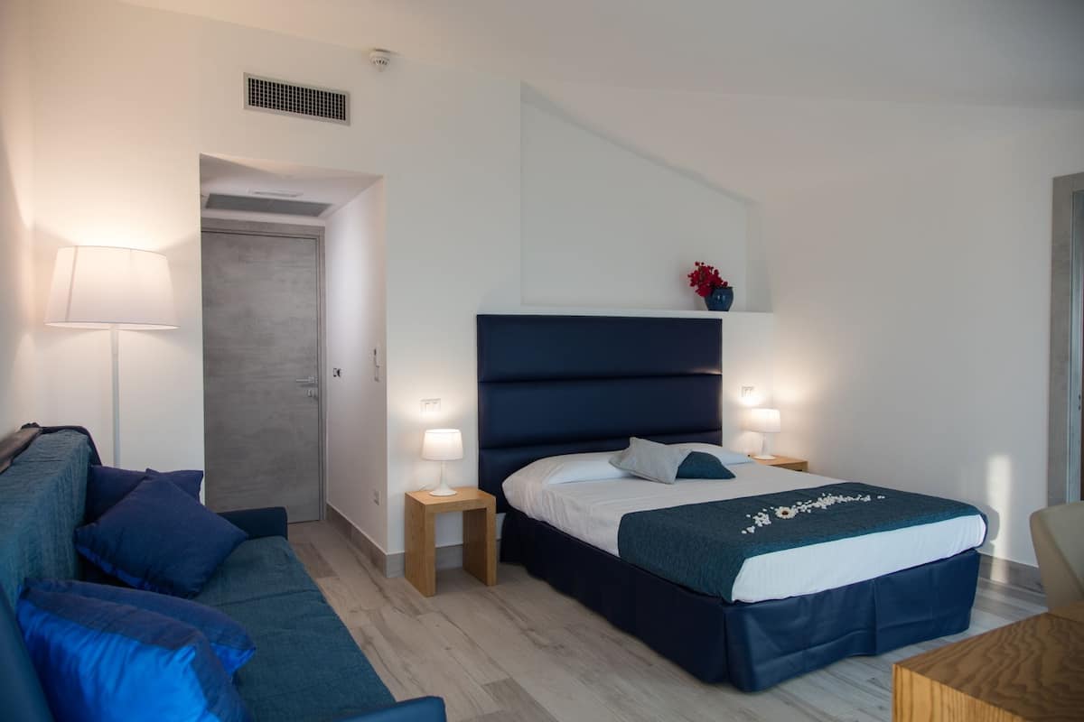 A modern bedroom with a bed, bedside tables, a nightstand, a lamp, a sofa, and a small table.
