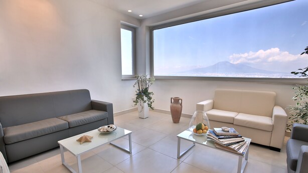A modern living room with a grey sofa, a white coffee table, and a beige sofa. There is a large window with a view of a mountain. - Relais Manfredi (Castellammare di Stabia)