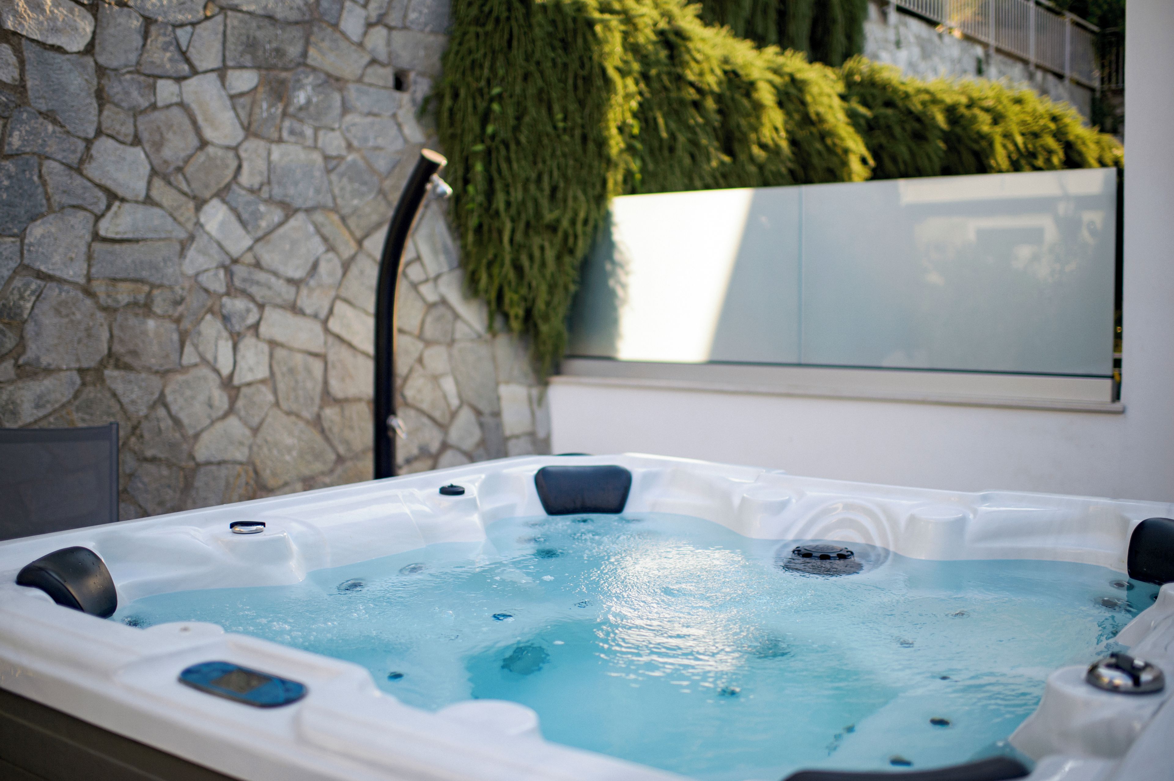 A hot tub with a stone wall and greenery in the background.