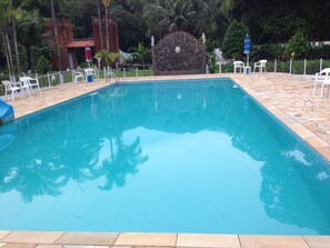 A rectangular pool with a stone border, surrounded by white plastic chairs and a stone wall with a statue. - Pousada Ecológica Cavalo de Pedra (Peruíbe)