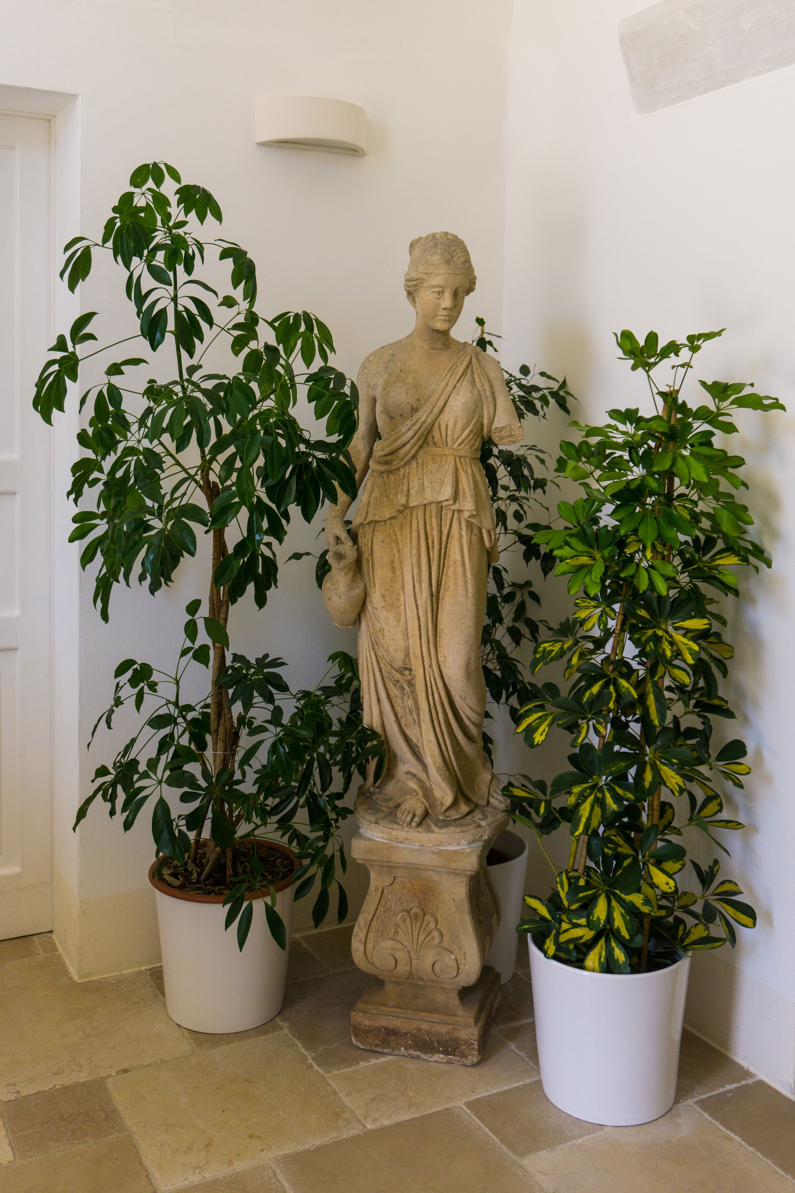 Una estatua de figura clásica flanqueada por dos plantas en macetas.