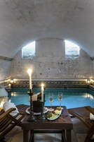 A dining table with candles, wine glasses, and plates of food in a room with a pool and arched ceiling.
