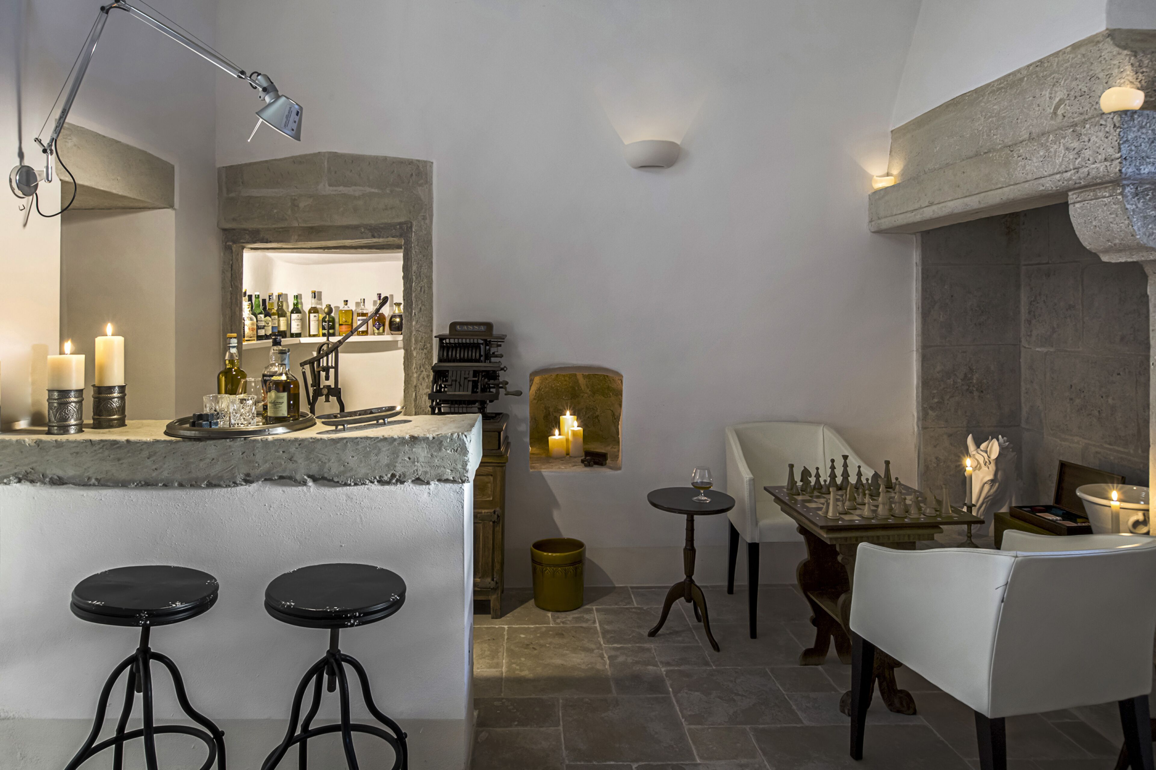 A bar area with stools, a chess table, and a shelf with bottles.