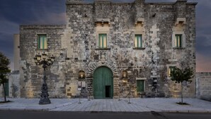 A historic stone building with a green arched entrance, multiple windows, and a street lamp in front.