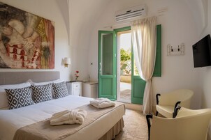 Ein Hotelzimmer mit Bett, einem Sessel, einem Gemälde, einem Fernseher und einer offenen Tür nach draußen.
