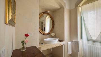 A bathroom with a white sink, a round mirror, a vase with flowers, and a towel rack.