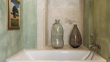 Un baño con un lavamanos blanco, dos botellas de vidrio y un cuadro en la pared.