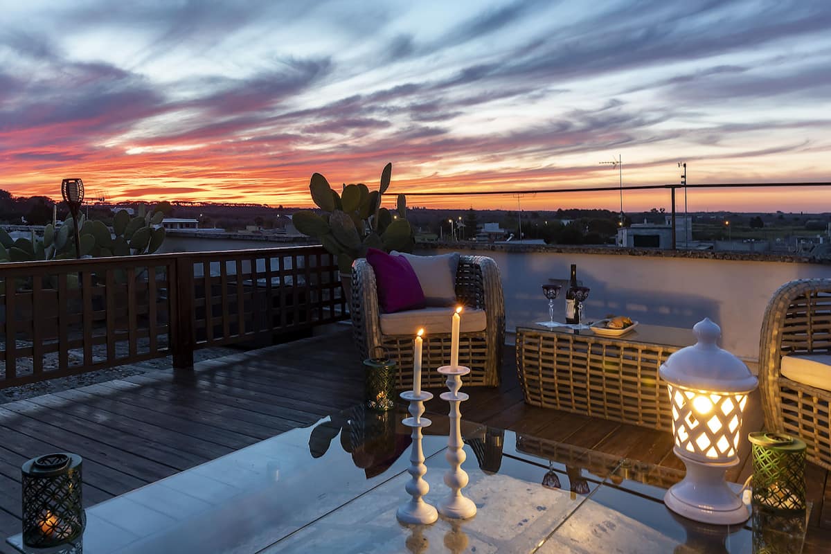 Une vue sur le coucher de soleil depuis une terrasse sur le toit, avec une table, deux bougies et des meubles en osier.