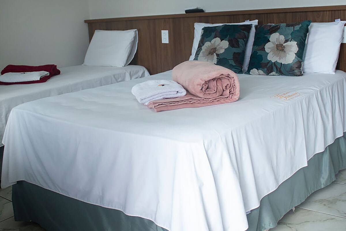 Quarto de hotel com duas camas, um quadro de flores na parede e piso de azulejos.