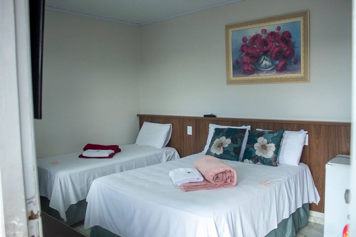 Quarto de hotel com duas camas de solteiro, um quadro de flores na parede e um armário branco.