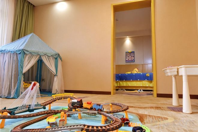 A room with a play area featuring a train set, a tent, and a bed with a blue bedspread.