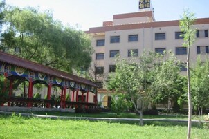 Un edificio con estilo arquitectónico tradicional, un espacio al aire libre cubierto con pilares rojos y un césped bien cuidado.