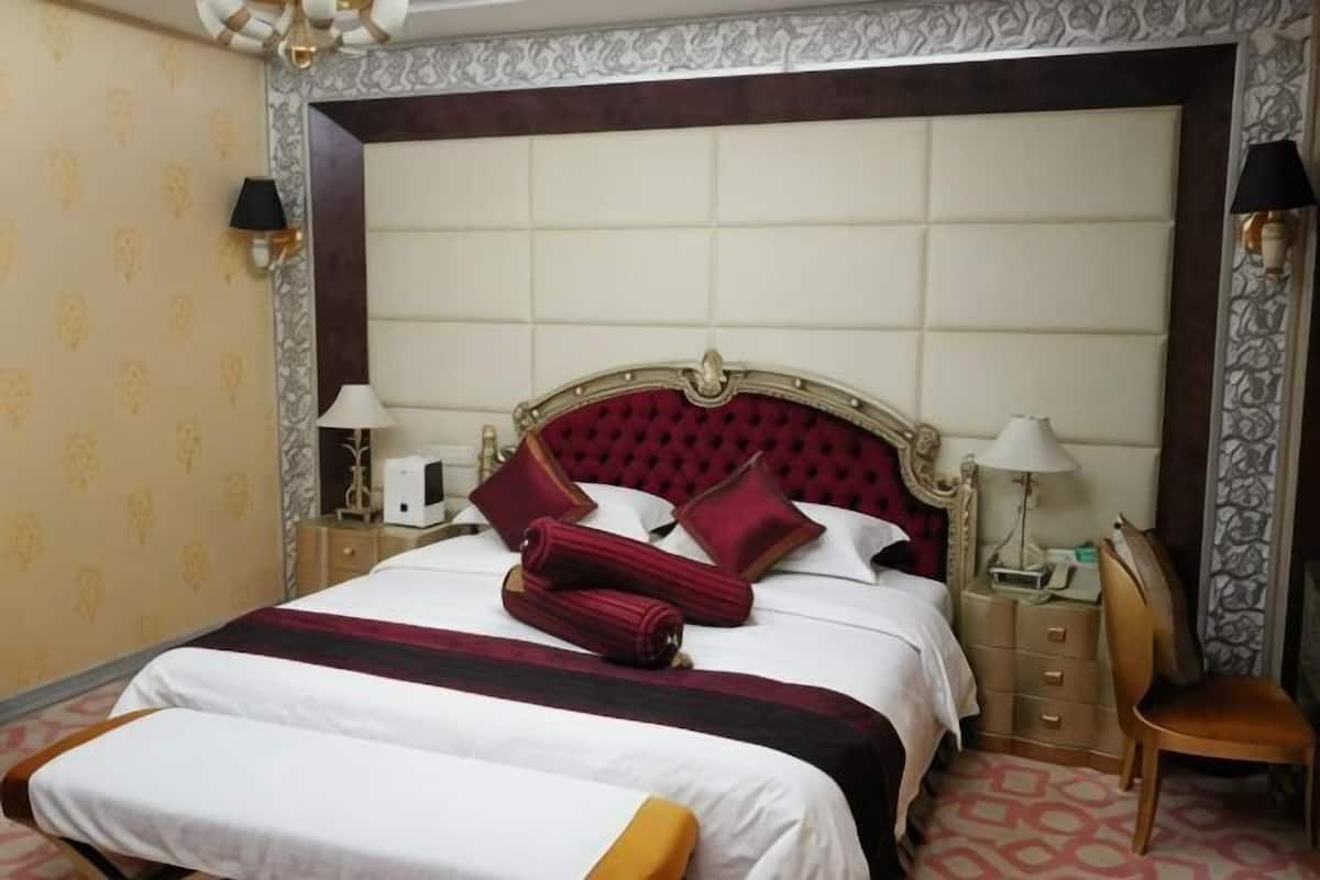A hotel room with a large bed, two bedside tables, a chair, and a decorative headboard.