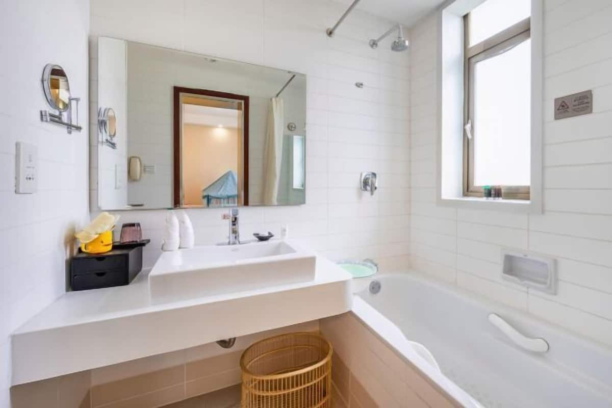A bathroom with a white sink, a mirror, a bathtub, and a window.