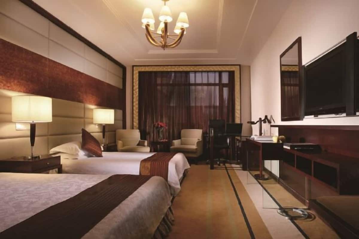 A hotel room with two beds, a desk, a chair, a TV, and a large window.
