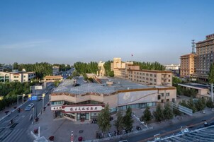 Un edificio de varios pisos con techo plano, rodeado de árboles y otros edificios.