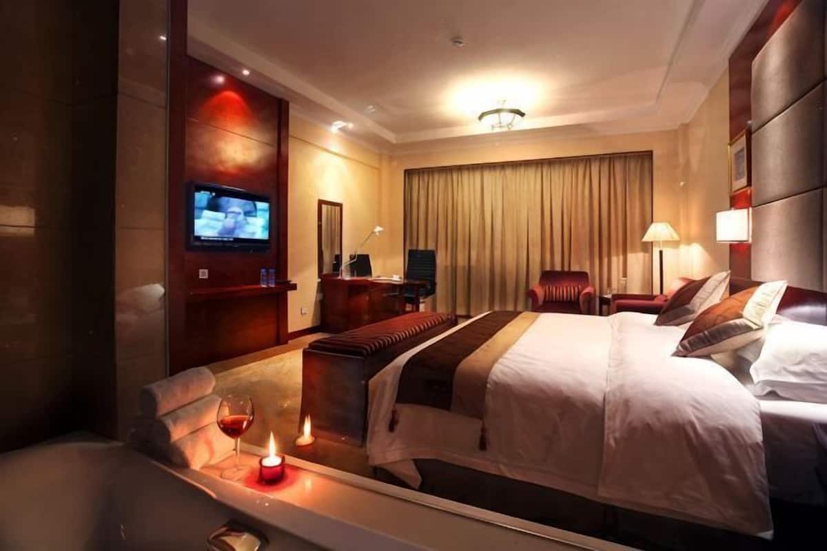 A hotel room with a large bed, a TV, a desk, and a chair.