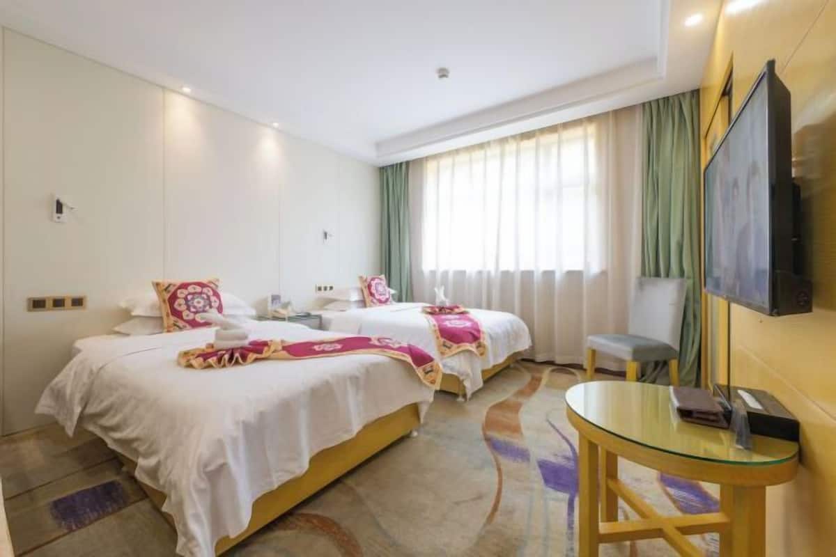A hotel room with two beds, a TV, a small table, and a window with curtains.
