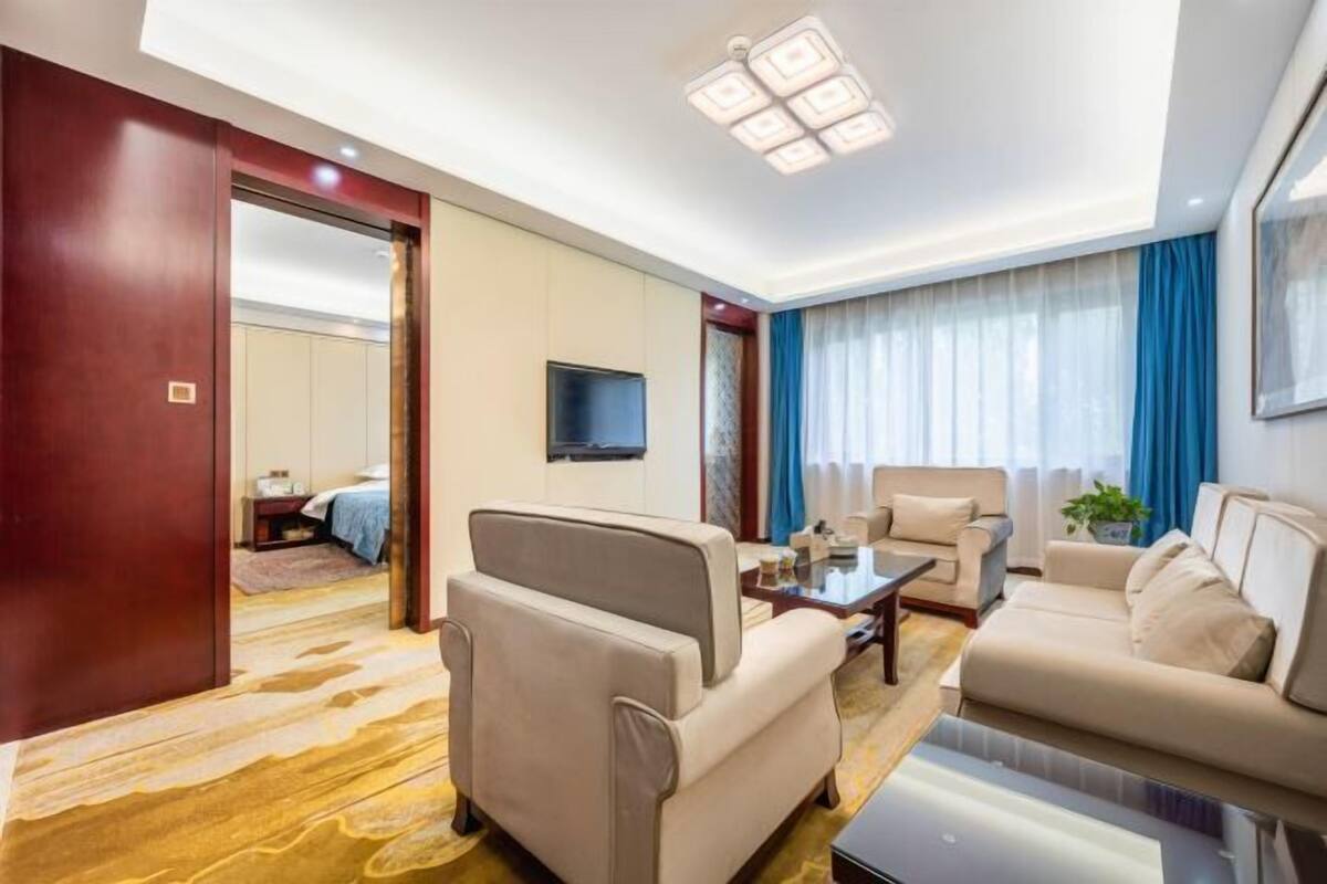 A modern hotel room with a sofa, armchair, and a flat-screen TV.