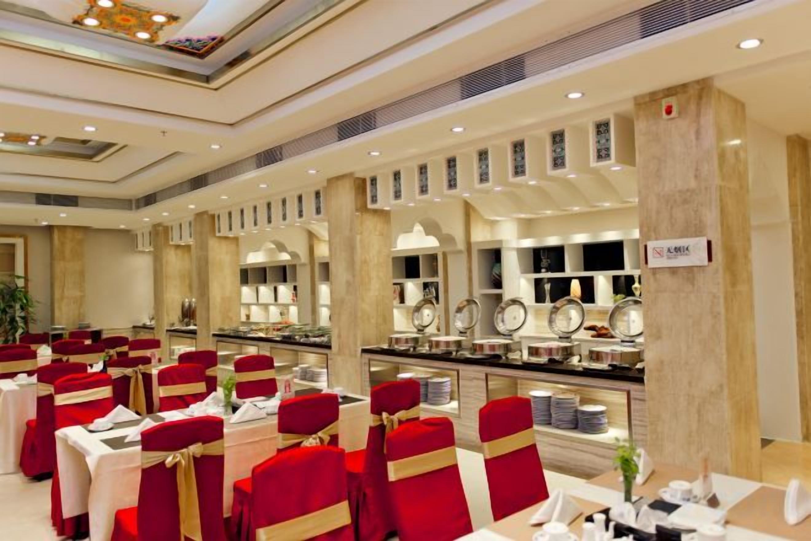 A banquet hall with round tables, red chairs, and a buffet area.