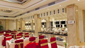 A banquet hall with round tables, red chairs, and a buffet area.