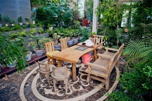 Un jardín interior con una mesa y sillas de madera rodeado de plantas en macetas.