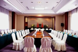 Un salón de conferencias con una larga mesa, sillas blancas y piso alfombrado.