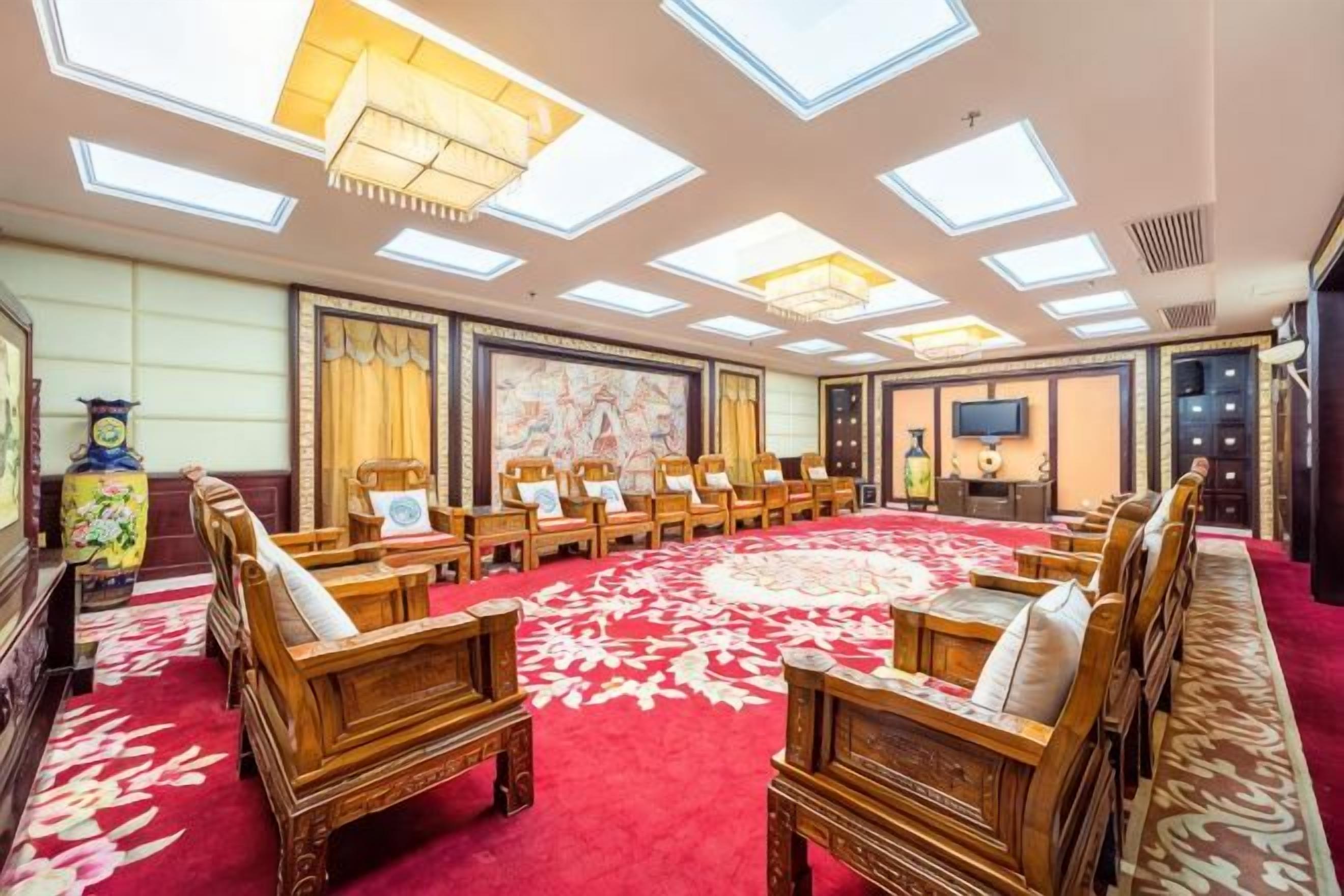 Un salón de conferencias con alfombra roja, sillas de madera, una gran mesa redonda y un techo con tragaluces.