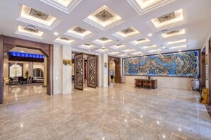Un amplio vestíbulo con piso de mármol, un mostrador de recepción y un gran elemento decorativo en la pared.