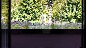 A balcony with two chairs and a small table, overlooking a garden with trees and purple flowers. - Maison Decoret (Vichy)