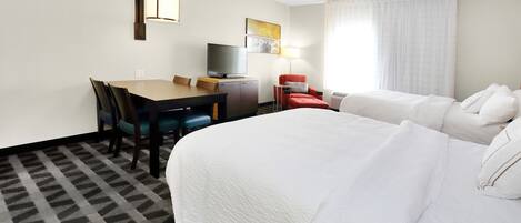 A hotel room with a large bed, a desk with a TV, and a chair.