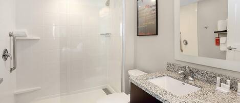 A modern bathroom with a glass-enclosed shower, a white toilet, and a granite countertop sink.