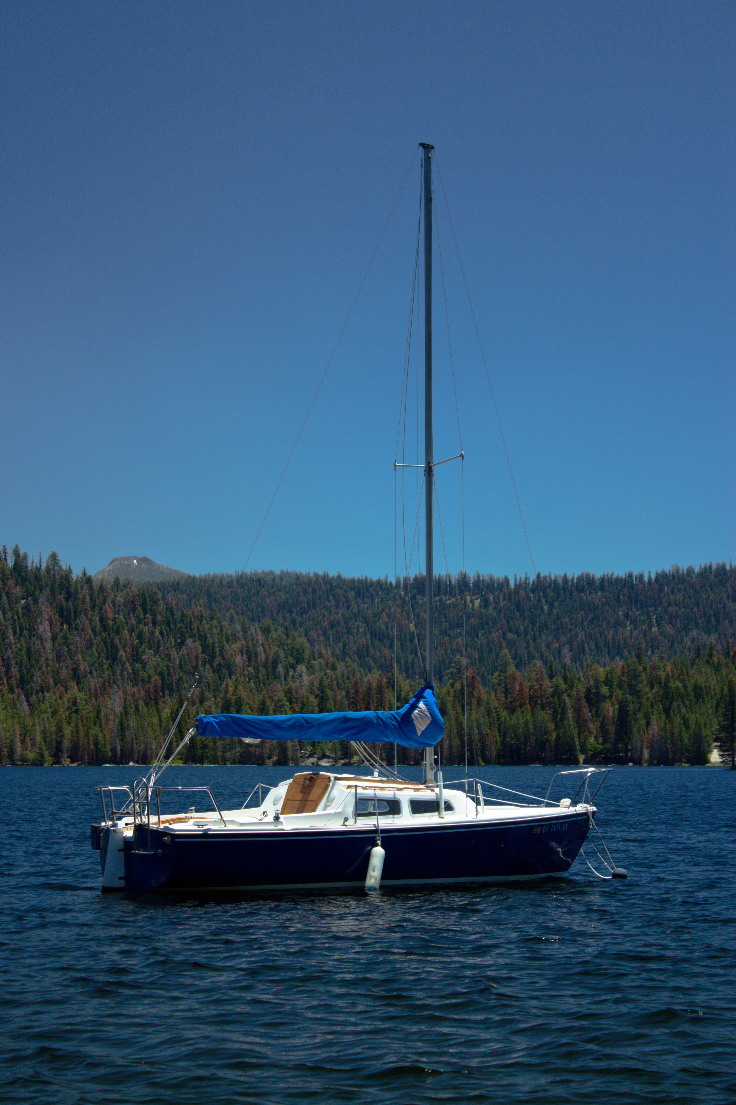 A sailboat on calm water with a forested mountain in the background.