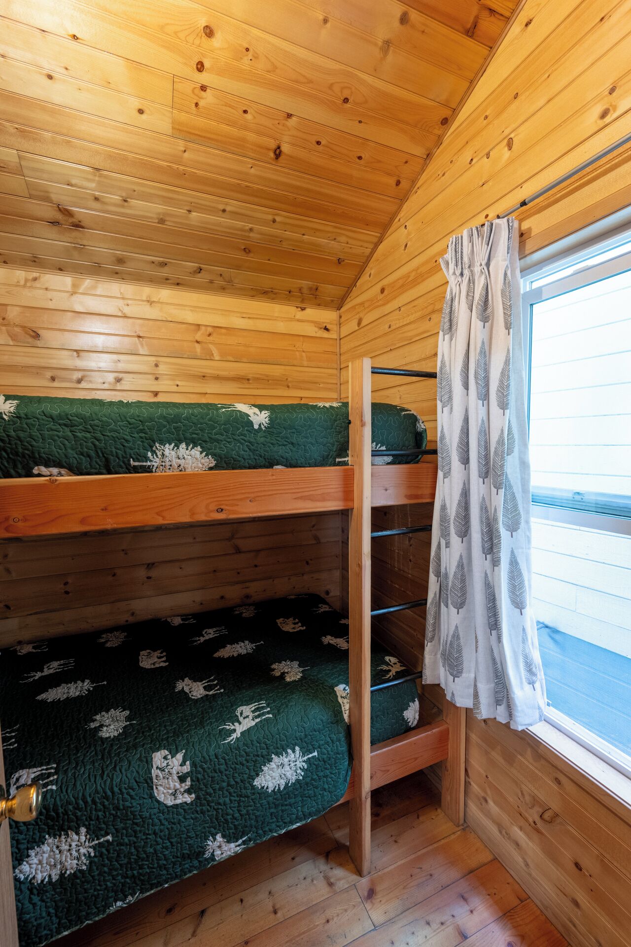 A bunk bed room with wooden walls and a window with curtains.