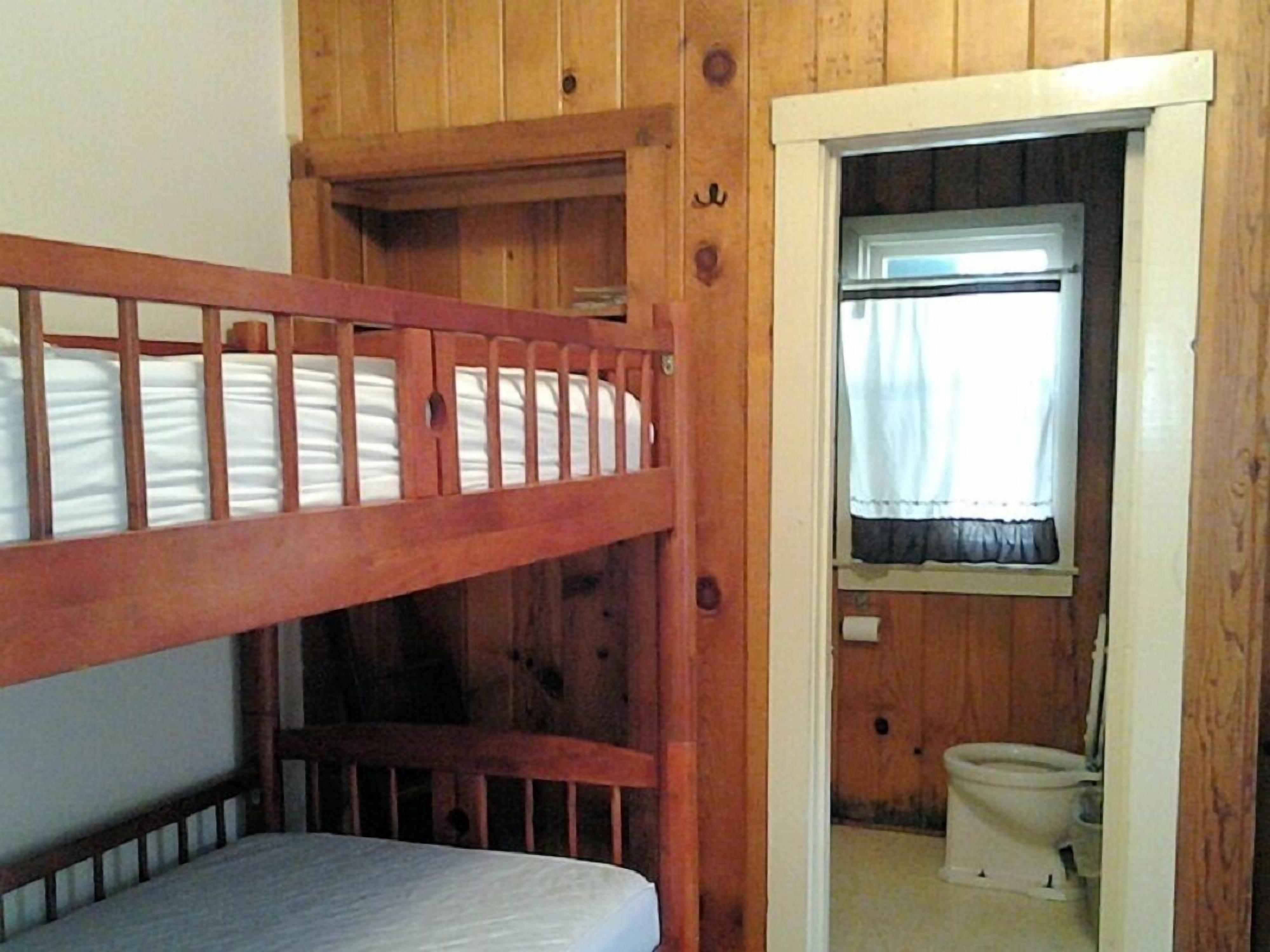 Un lit superposé dans une pièce en bois, avec une petite salle de bain visible à travers une porte ouverte.