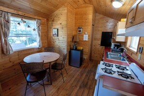 A wooden cabin interior with a dining table, chairs, a refrigerator, a stove, and a sink. - Huntington Lake Resort - Campsite (Lakeshore)