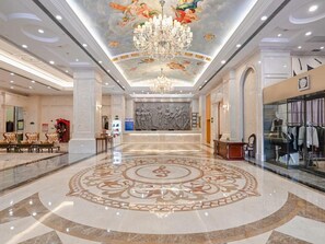 A spacious lobby with a grand chandelier, a central decorative floor pattern, and a clothing store on the right.